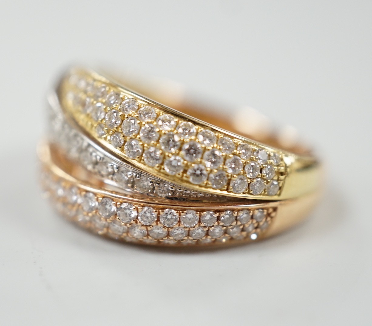A modern three colour 18ct gold and diamond chip cluster set three row crossover ring, size O, gross weight 6.9 grams.